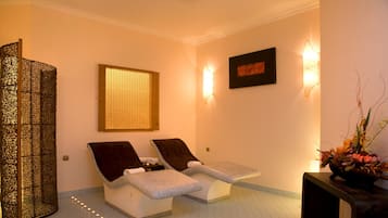 A spa room with two reclining chairs, a decorative screen, a wall-mounted light fixture, and a framed artwork.