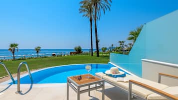 Un espace aménagé au bord de la piscine, avec vue sur l’océan, comprenant une chaise longue et une table avec un verre et des lunettes de soleil.
