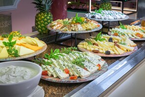 A buffet with various cheeses, fruits, and a bowl of dip.