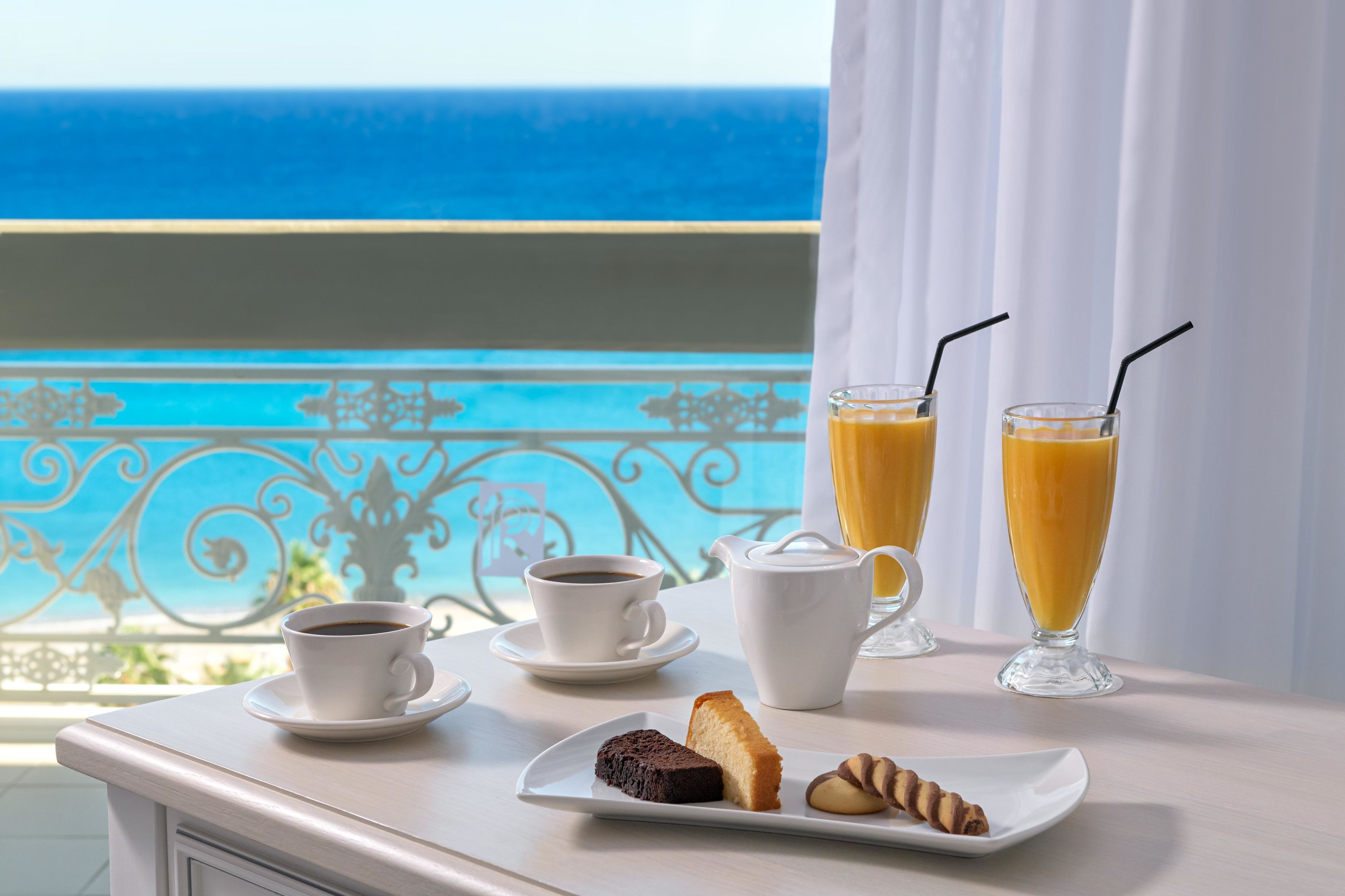 Un plateau de petit-déjeuner avec du café, du jus de fruits et des viennoiseries, installé sur un balcon donnant sur la mer.