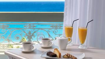 Un plateau de petit-déjeuner avec du café, du jus de fruits et des viennoiseries, installé sur un balcon donnant sur la mer.