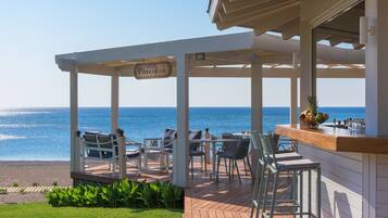 A covered outdoor seating area with a view of the ocean, a bar, and a sign reading "Poseidon".