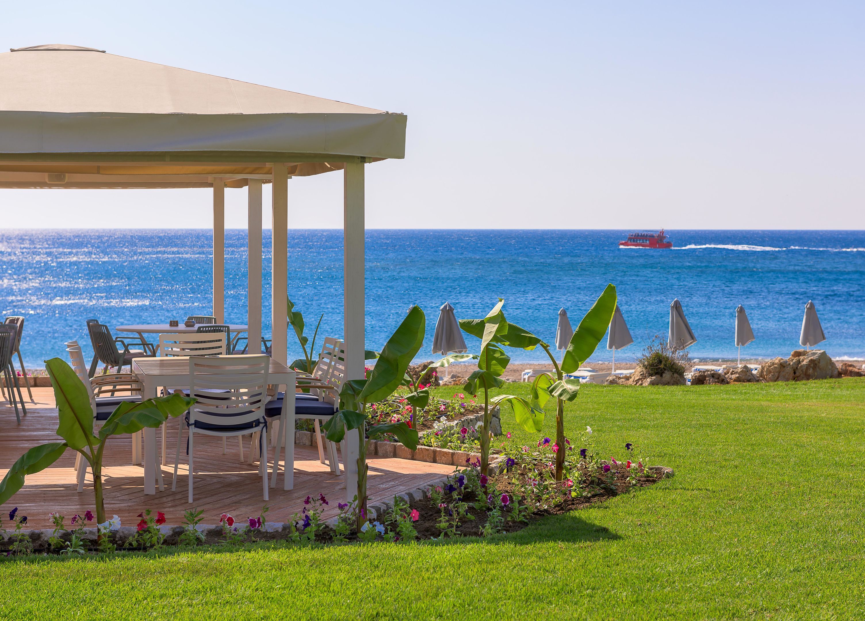 A covered outdoor seating area with tables and chairs, overlooking the sea.