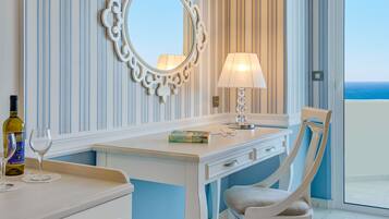 Habitación de hotel con escritorio blanco, una silla, un espejo, una lámpara y vista al océano.