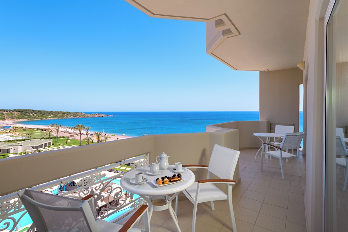 A balcony with a table set for two, a chair, and a view of the ocean.