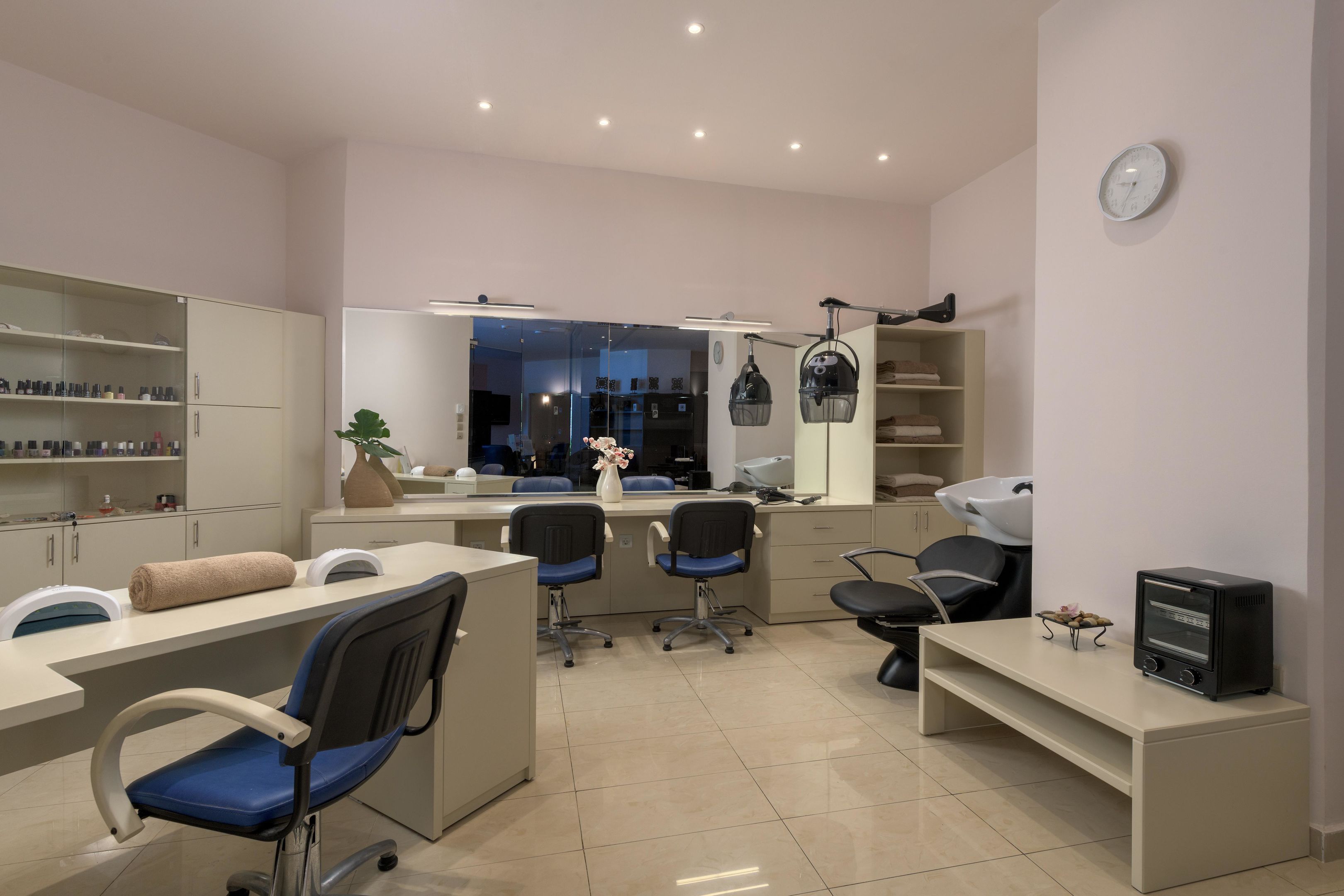 A modern salon with a reception desk, chairs, shelves with products, a mirror, and a clock on the wall.