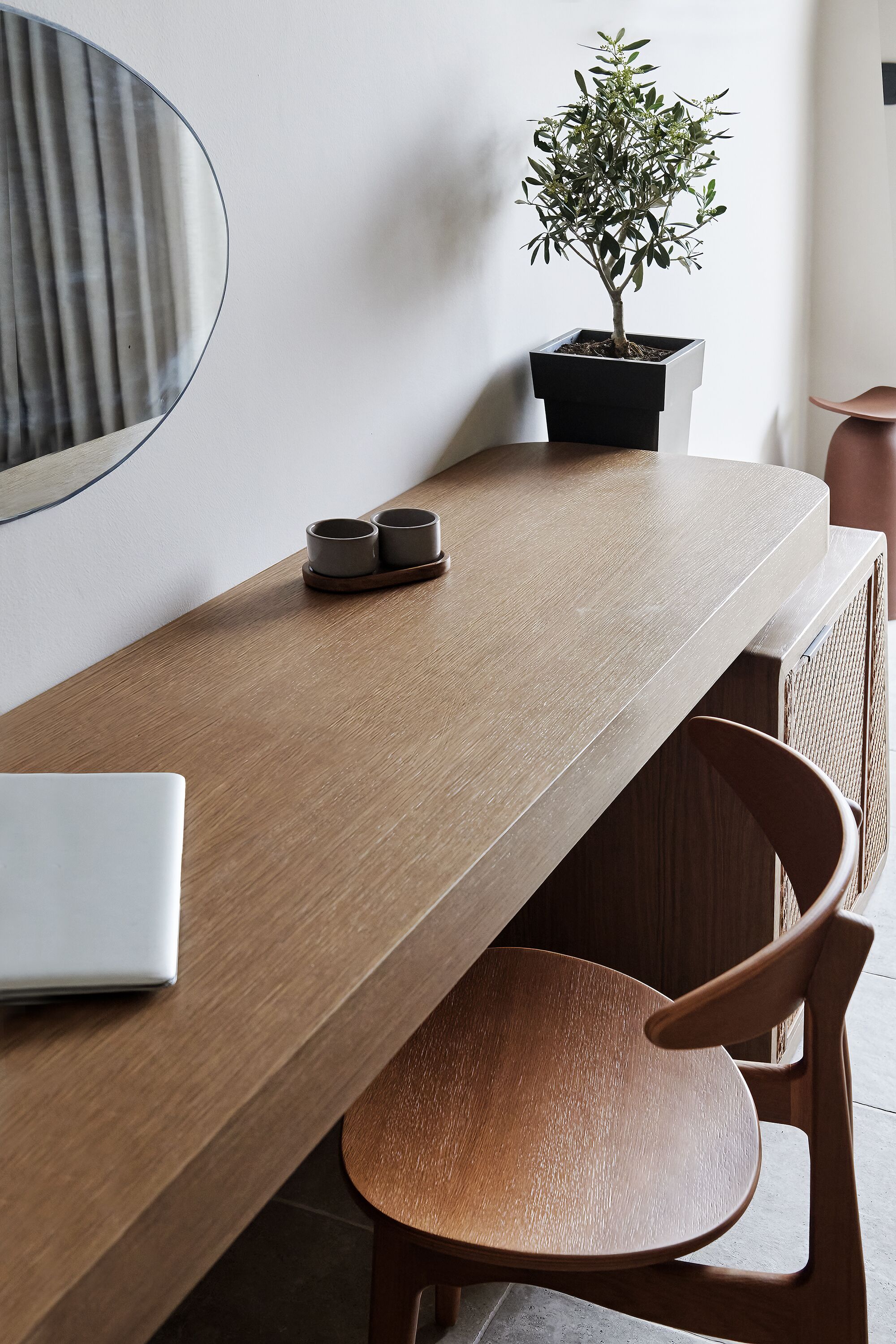 A wooden table with a laptop and two cups, a potted plant, and a chair.