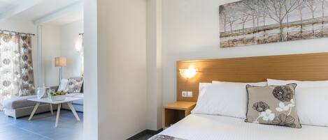 A hotel room with a bed, a nightstand, a lamp, a painting on the wall, and a view of the room through an open door.