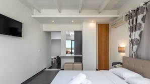 A hotel room with a bed, a TV mounted on the wall, a desk, and a bathroom visible through an open door. - City Center Hotel (Rhodes)