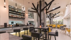 A modern bar area with a high ceiling, exposed beams, and a variety of seating options including bar stools and tables. - City Center Hotel (Rhodes)
