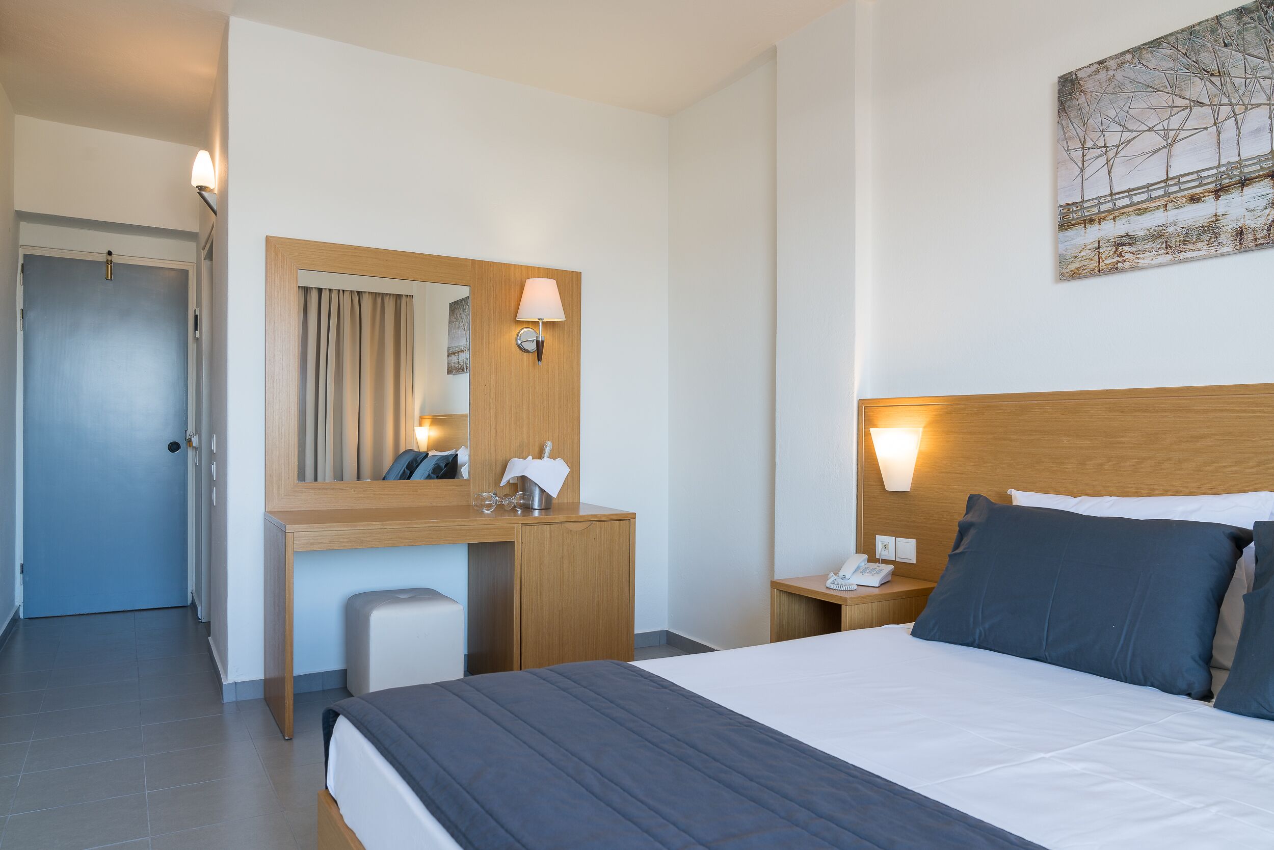 Ein Hotelzimmer mit Bett, Schreibtisch mit Spiegel, Nachttisch und Tür.