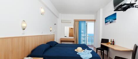 A hotel room with two beds, a desk, a chair, a TV, and a view of the sea.
