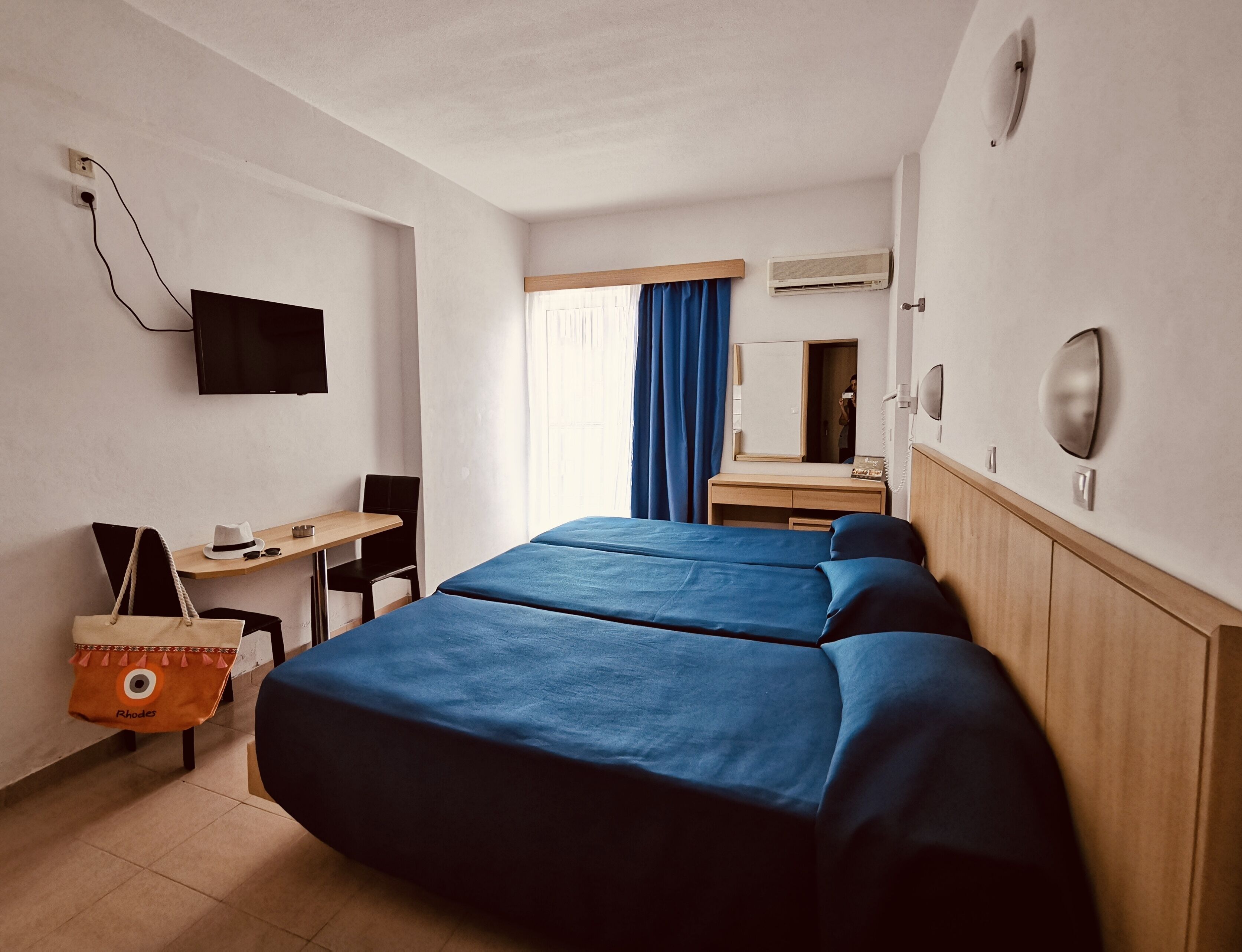A hotel room with two beds, a desk, a chair, a television, a mirror, and a telephone.