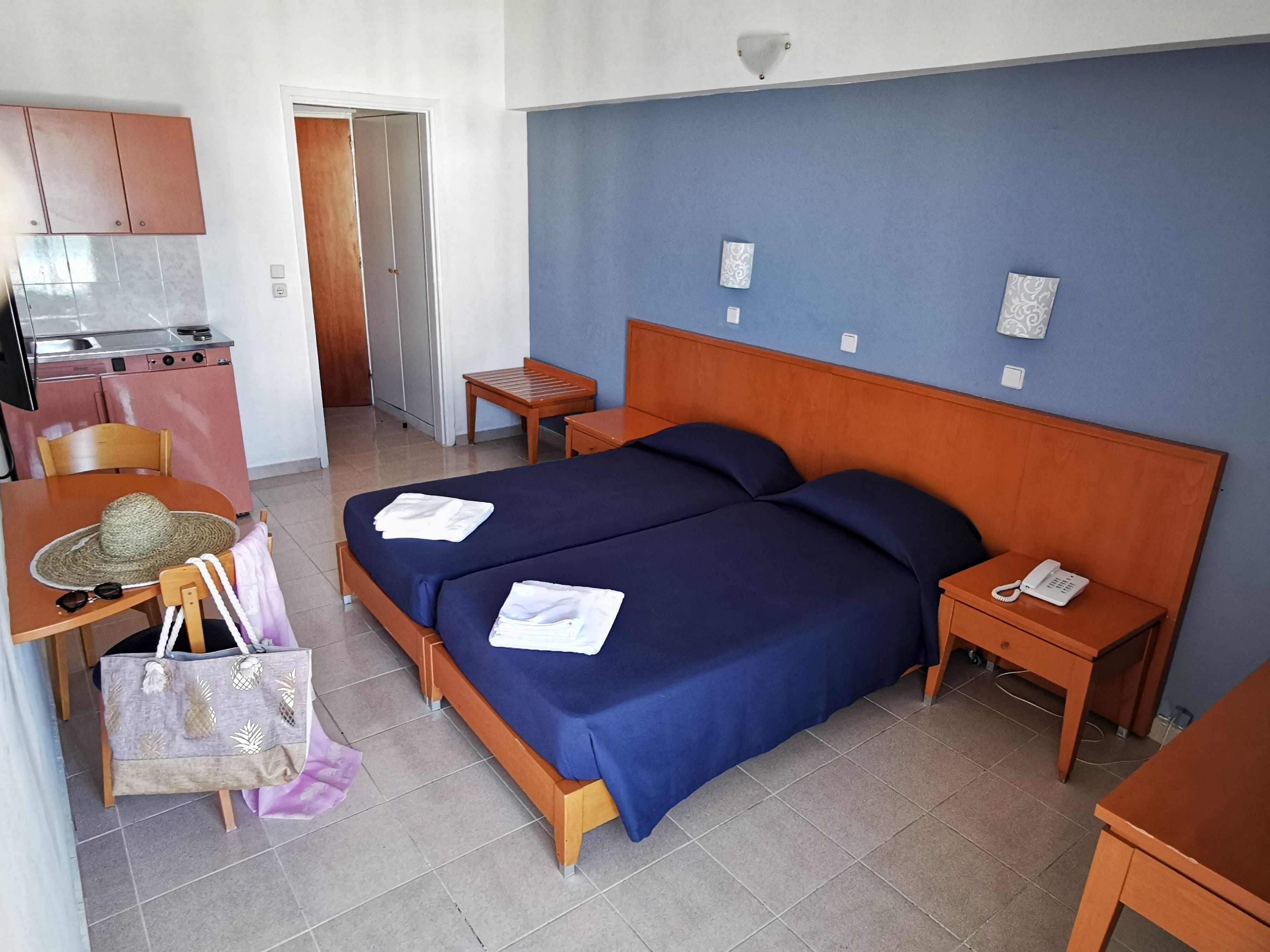 A hotel room with a bed, bedside tables, a desk with a chair, a kitchenette, and a bathroom.