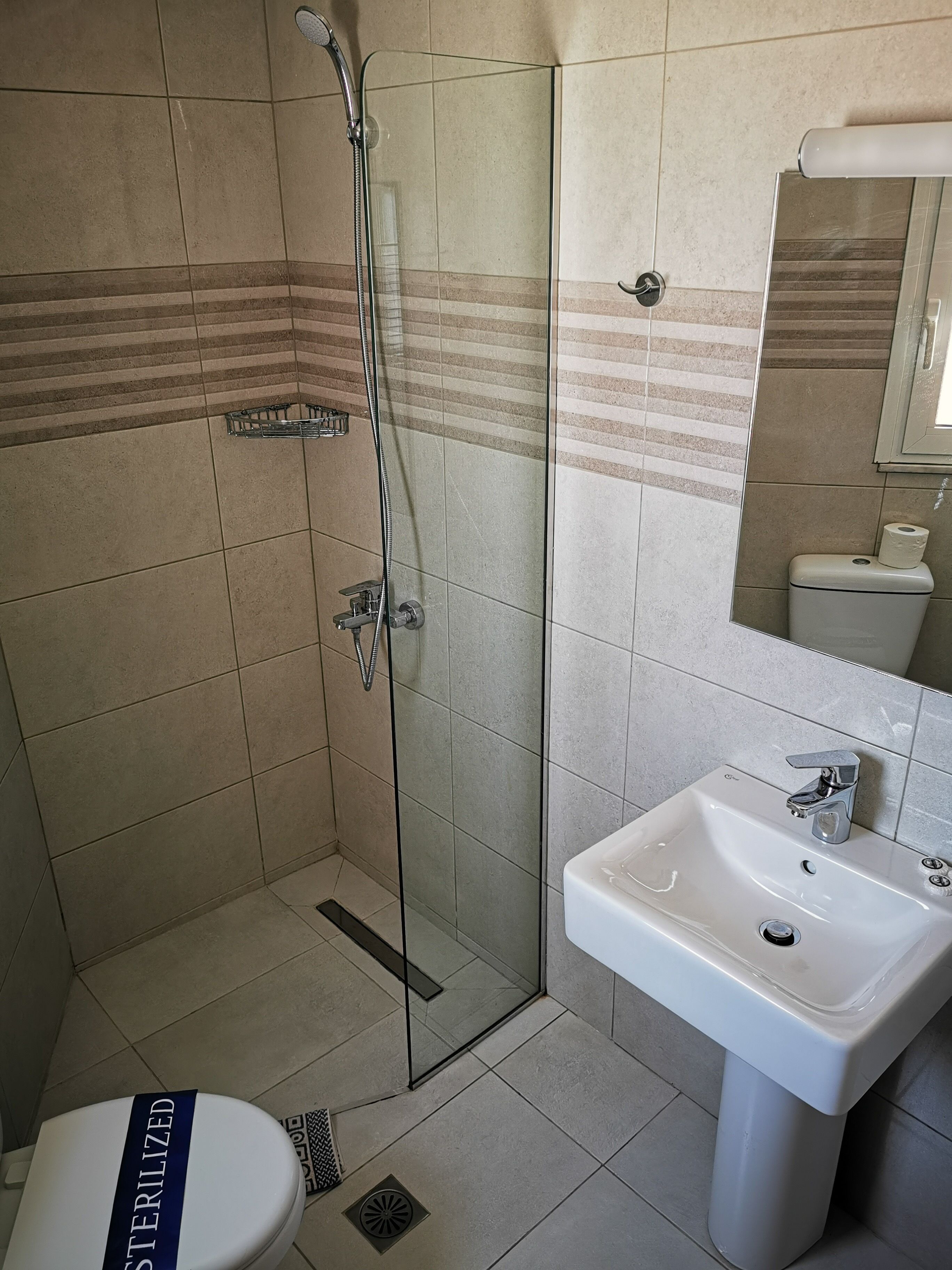 A bathroom with a glass-enclosed shower, a white sink, and a toilet with a "STERILIZED" label.