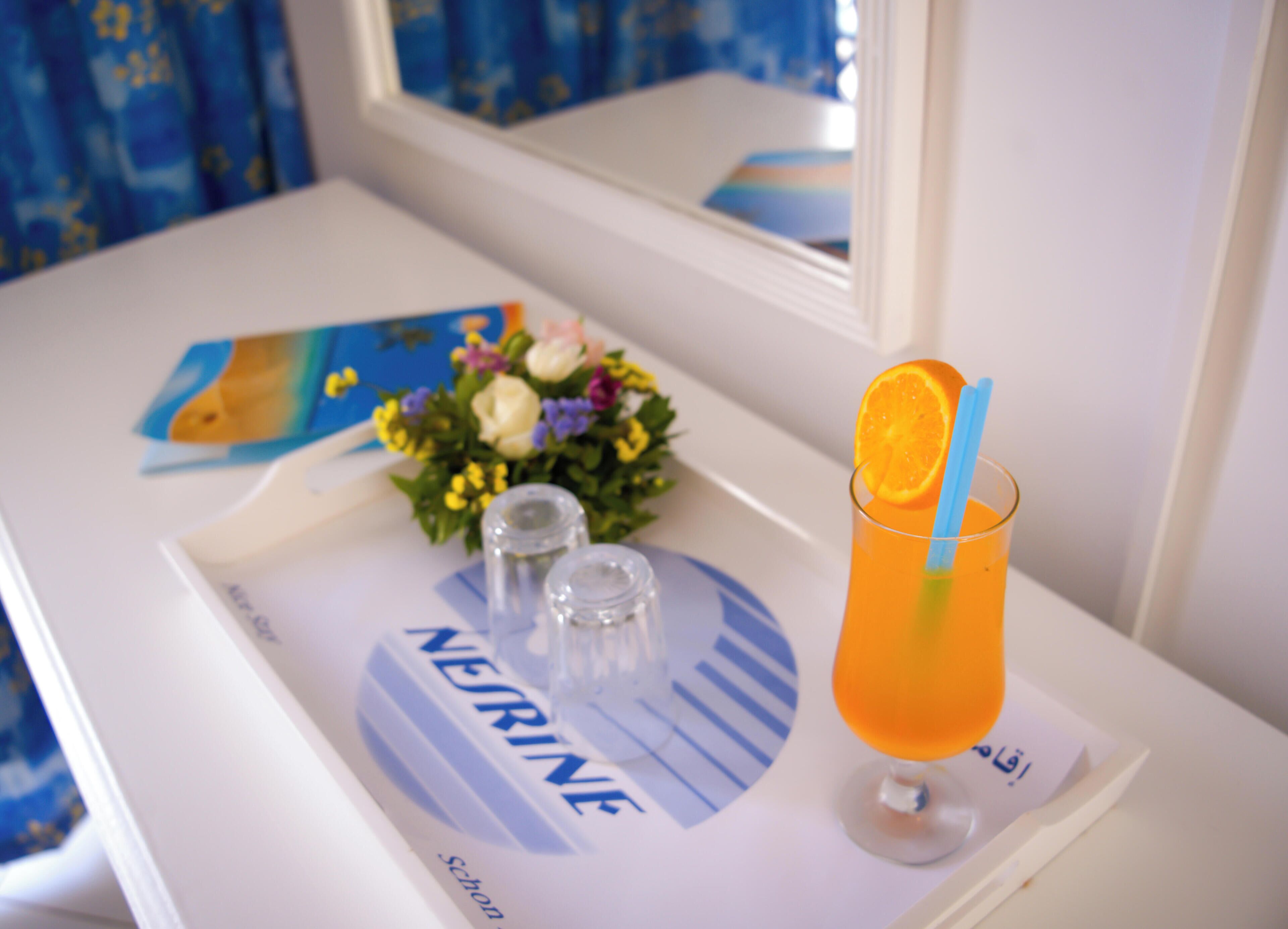 Ein Tablett mit einem Glas Orangensaft, einem kleinen Blumenstrauß und Salz- und Pfefferstreuern auf einem wei ßen Tisch.