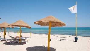 Ein Strand mit Strohdächern, Liegestühlen und einer Flagge.