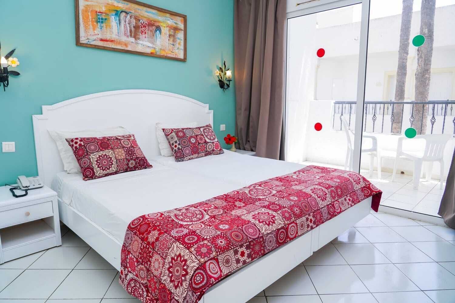 Un dormitorio con cama, una mesita de noche, un cuadro en la pared y vistas al balcón exterior.