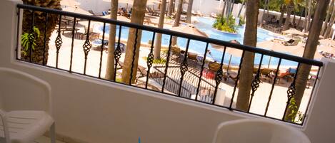 A balcony with a view of a pool area, including lounge chairs and umbrellas.