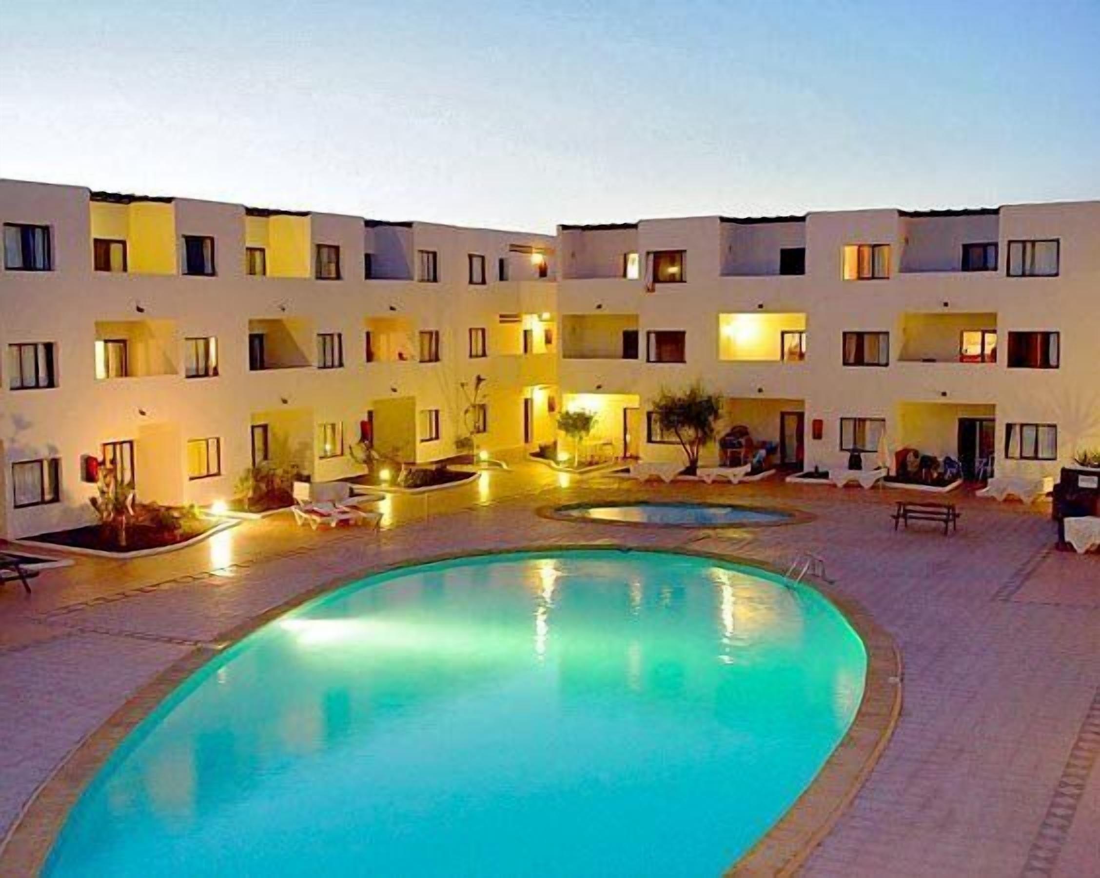 A hotel with a swimming pool, multiple balconies, and outdoor seating areas.