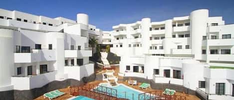 A modern hotel with white exterior walls, a central swimming pool, and multiple balconies.