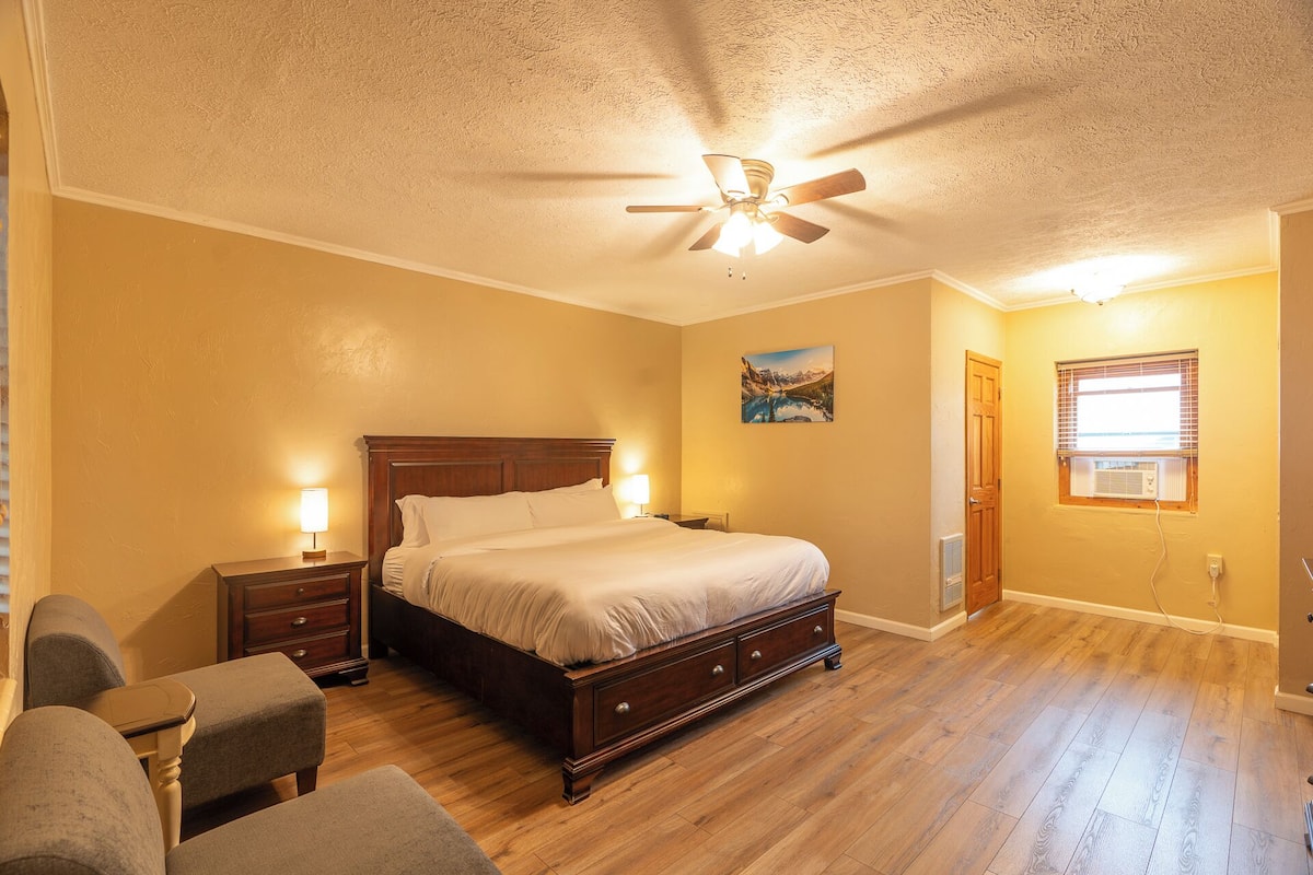 A bedroom with a wooden bed, two bedside tables with lamps, a ceiling fan, and a window with blinds.