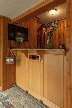 A wooden kitchen with a flat-screen TV mounted above the countertop, a vase with flowers on the counter, and a sign that reads "open".