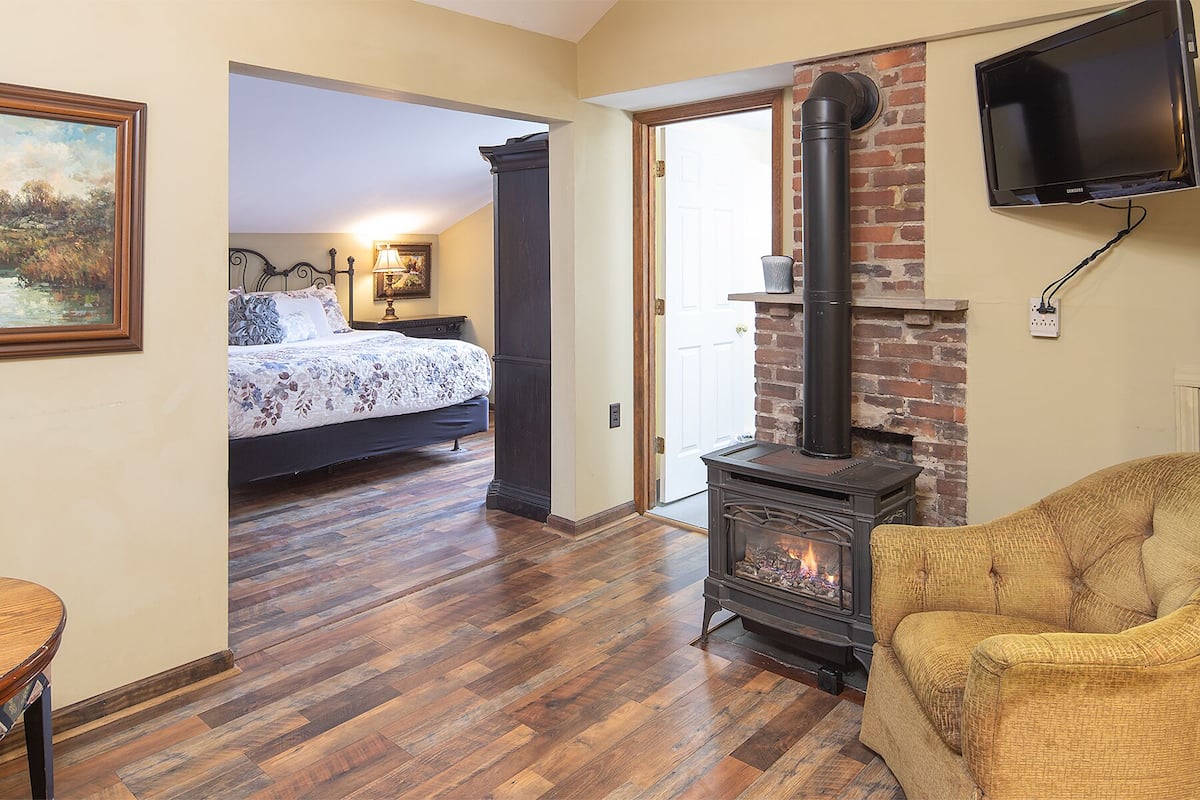 A cozy room with a wooden floor, a bed with floral bedding, a fireplace, and a television mounted on the wall.