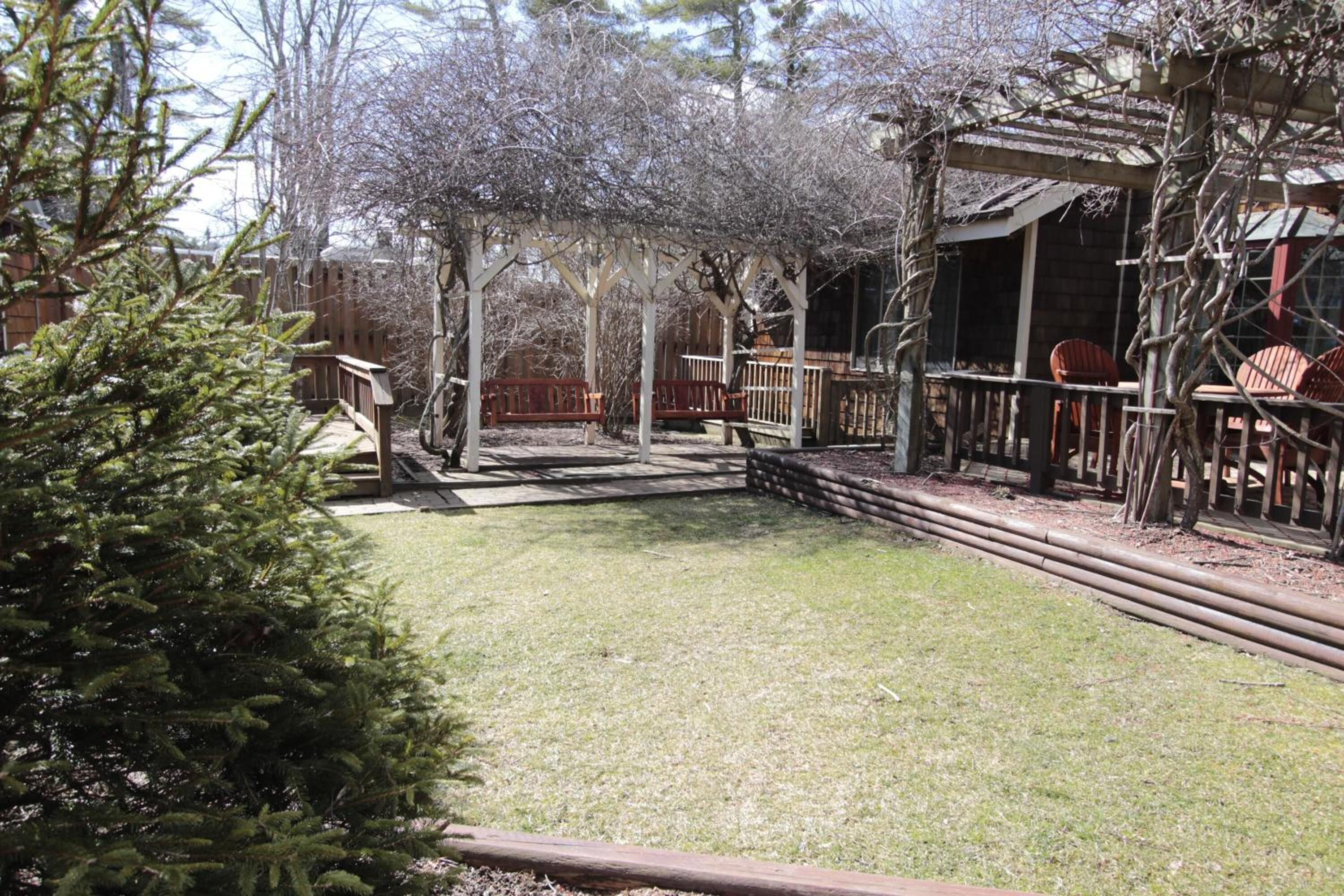 A wooden deck with a pergola, a small wooden structure, and a fenced area with chairs.