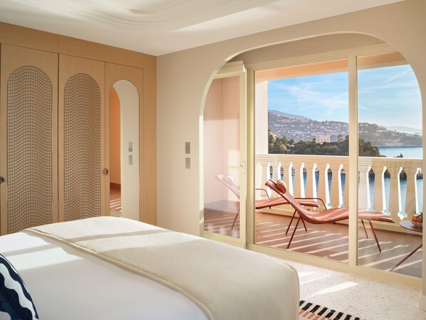 Un dormitorio con una cama grande, un balcón con vistas al mar y una puerta corredera con diseño decorativo.