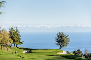 A golf course with a clear view of the ocean and a path leading to the tee area.
