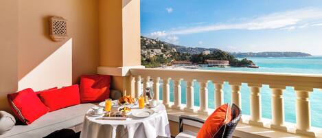 A balcony with a table set for breakfast, overlooking a coastal view.