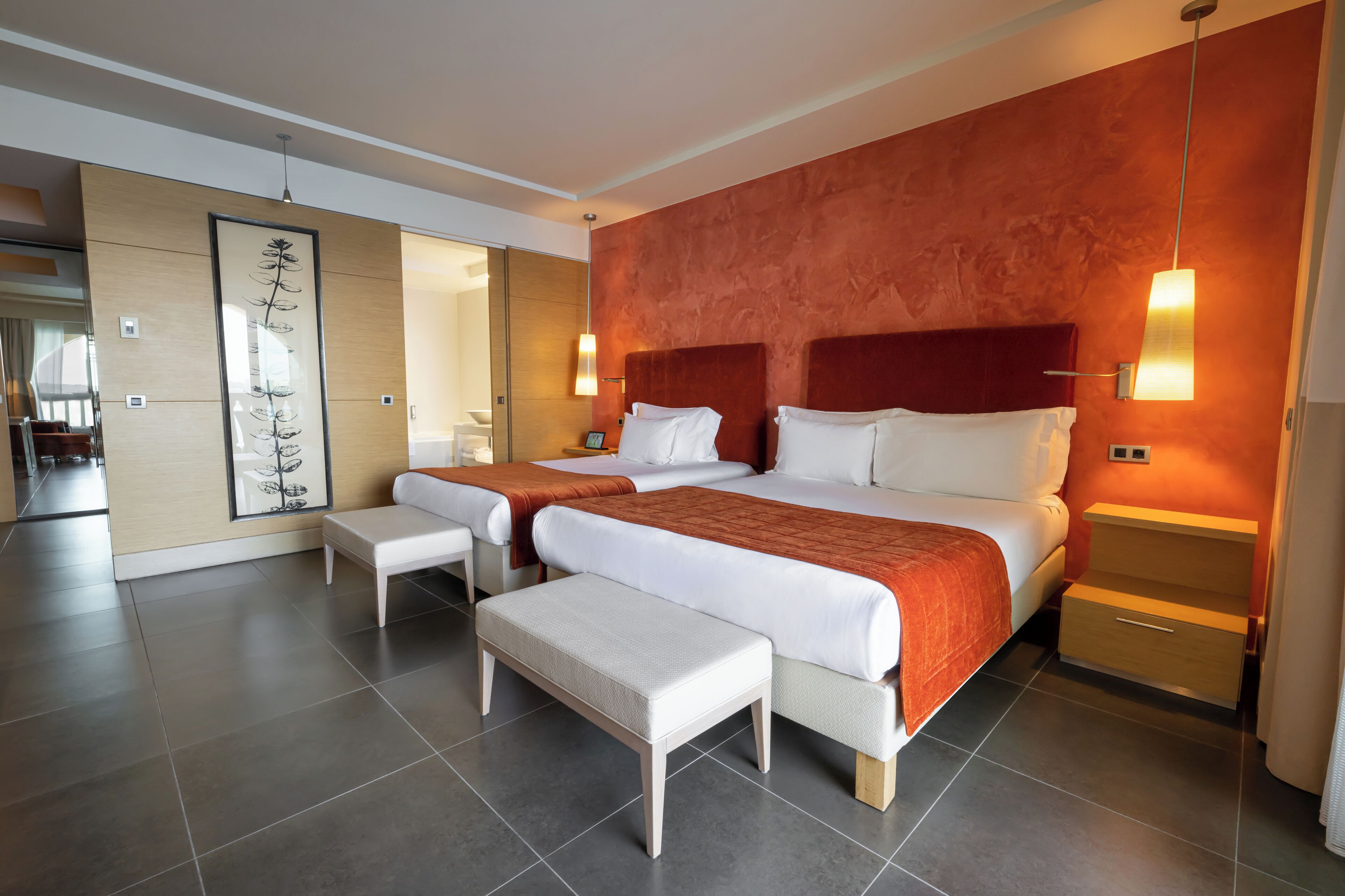 Una habitación de hotel moderna con dos camas, una obra de arte grande en la pared y un banco.