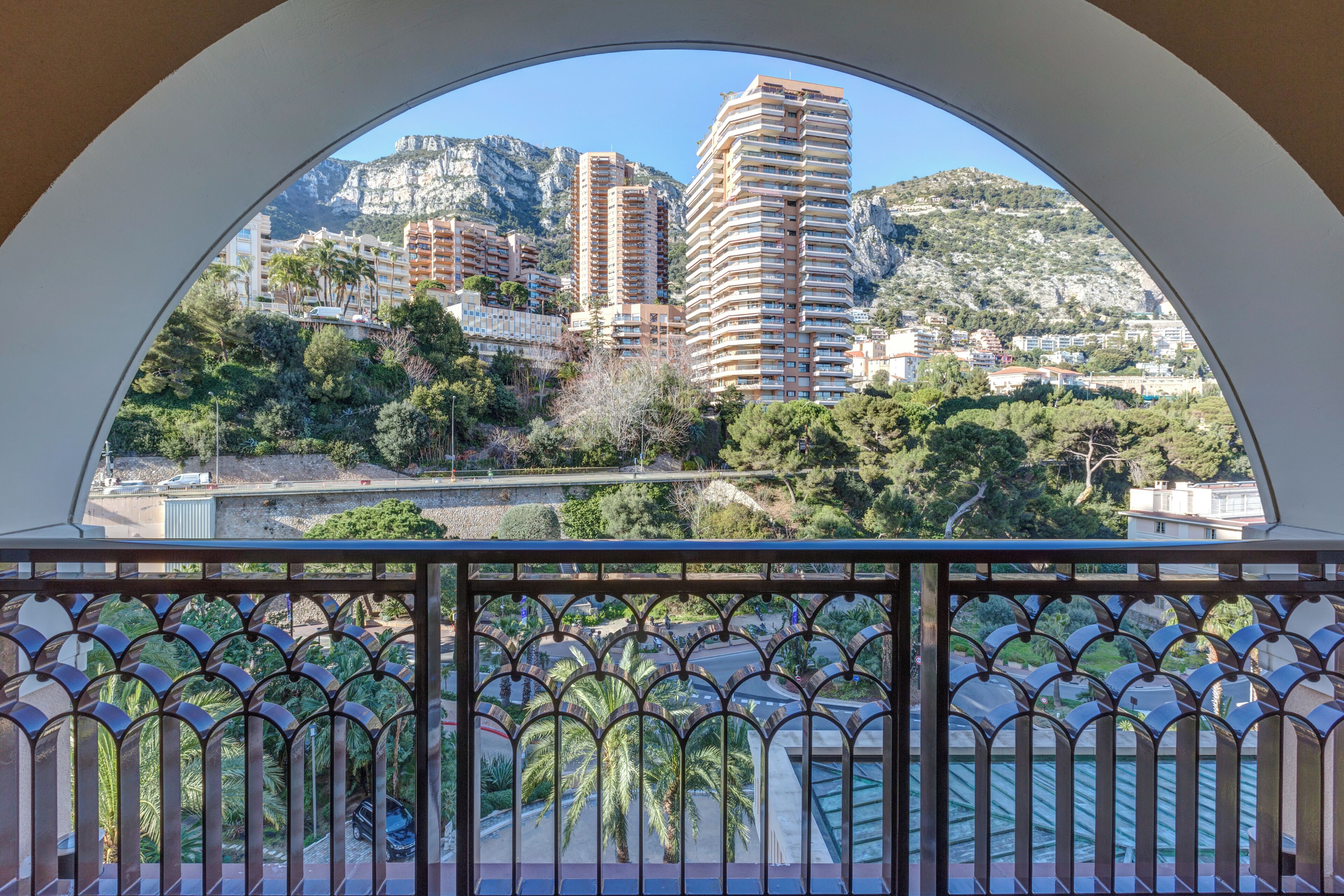 Vista da un balcone con ringhiera in metallo su un paesaggio urbano con palazzi alti, una montagna e vegetazione.