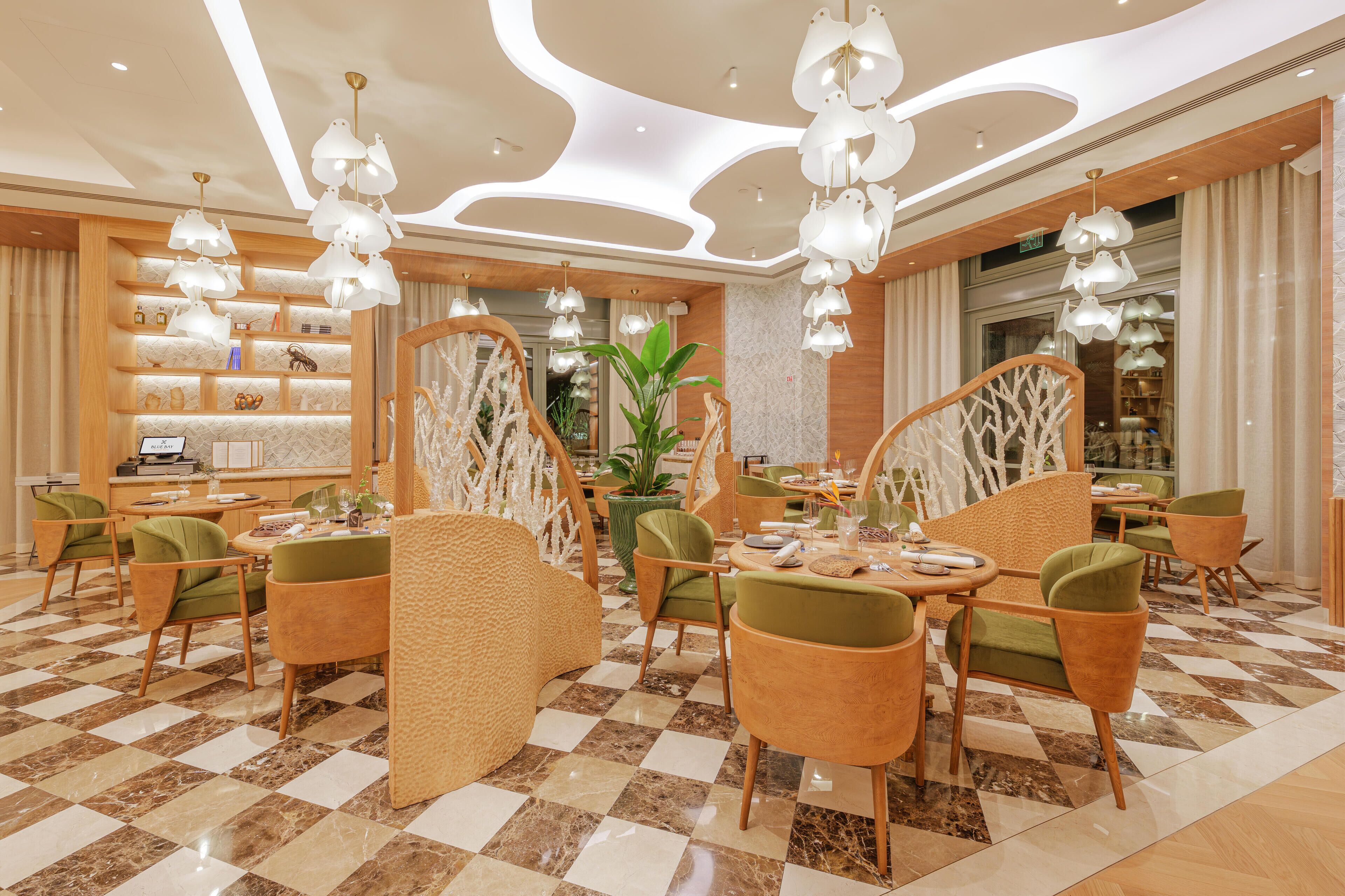A modern dining area with checkered flooring, green upholstered chairs, and white pendant lighting.