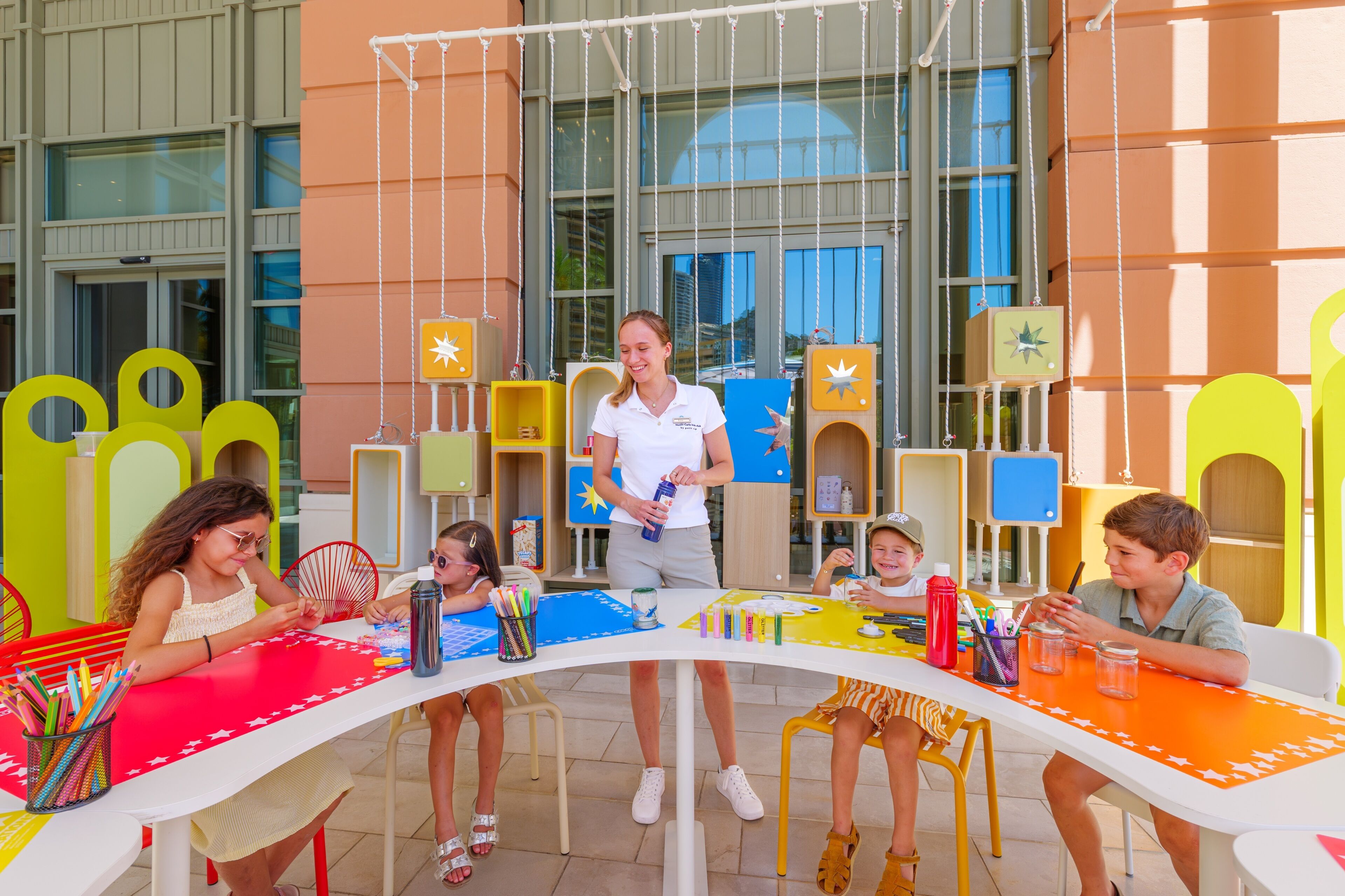 An outdoor seating area with colorful tables and chairs, a building with large windows, and a clear sky.
