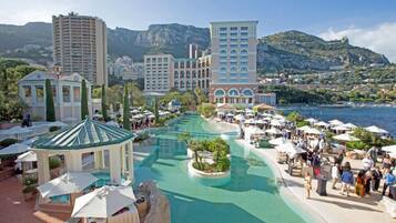 Um resort com piscina central, vários edifícios e montanhas ao fundo.