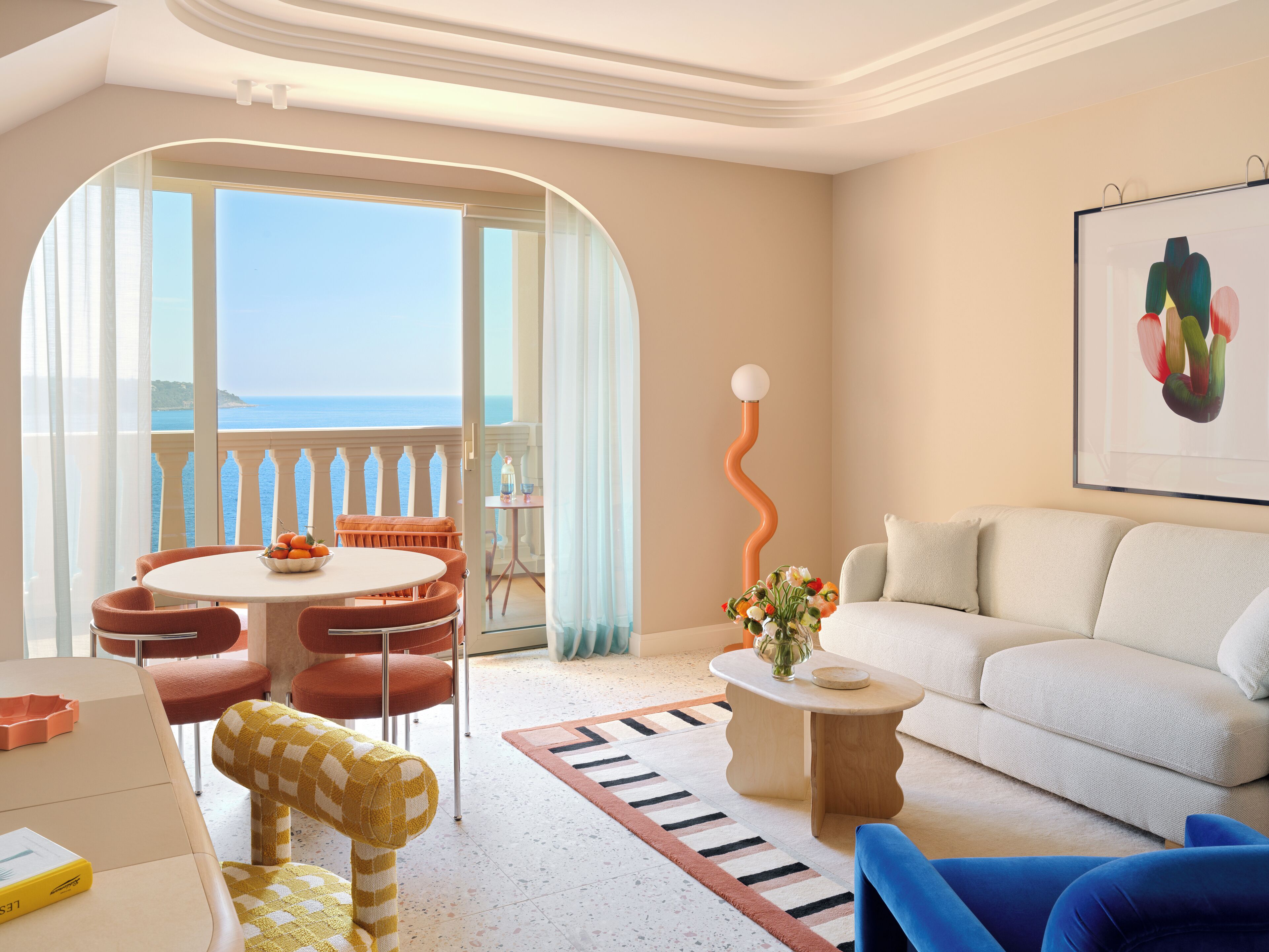 A modern living room with a view of the sea, a dining area with a table and chairs, and a unique orange floor lamp.