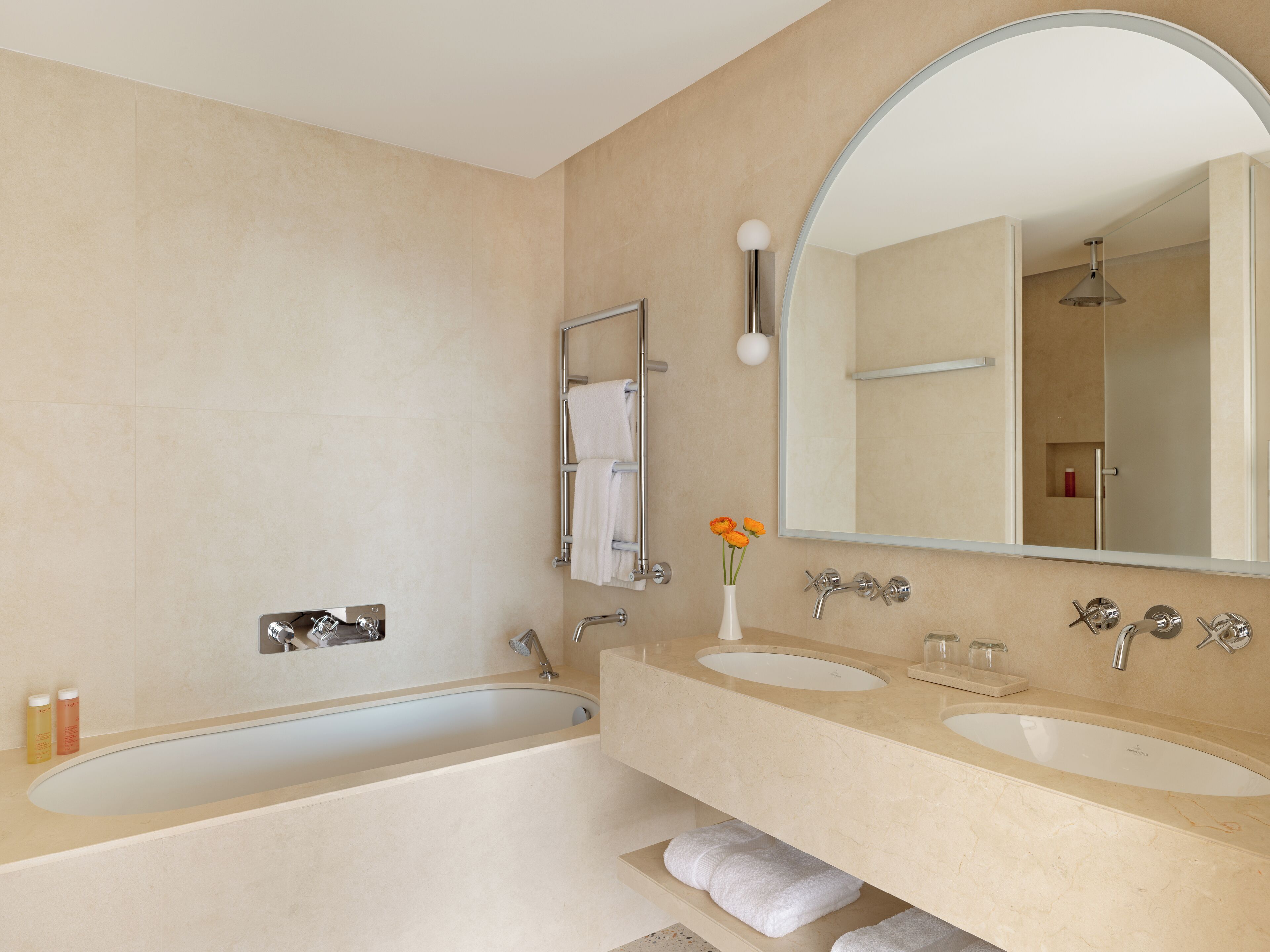 A modern bathroom with a bathtub, two sinks, a large mirror, and a towel rack.