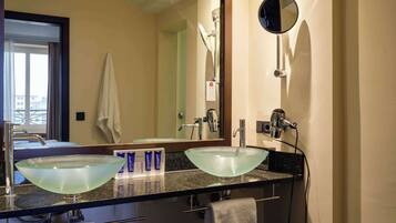Casa de banho com duas pias de vidro, um espelho grande e um secador de cabelo.