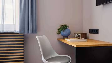 A modern room with a wooden desk, a white chair, a blue vase with a plant, a vintage radio, and a flat-screen TV mounted on the wall.
