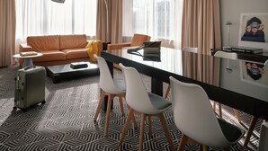 A modern hotel room with a sofa, a dining table with chairs, a suitcase, and a lamp. - Flemings Hotel München Schwabing (Munich)