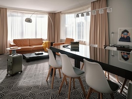 Quarto de hotel moderno com sofá, mesa de jantar com cadeiras, mala e luminária.