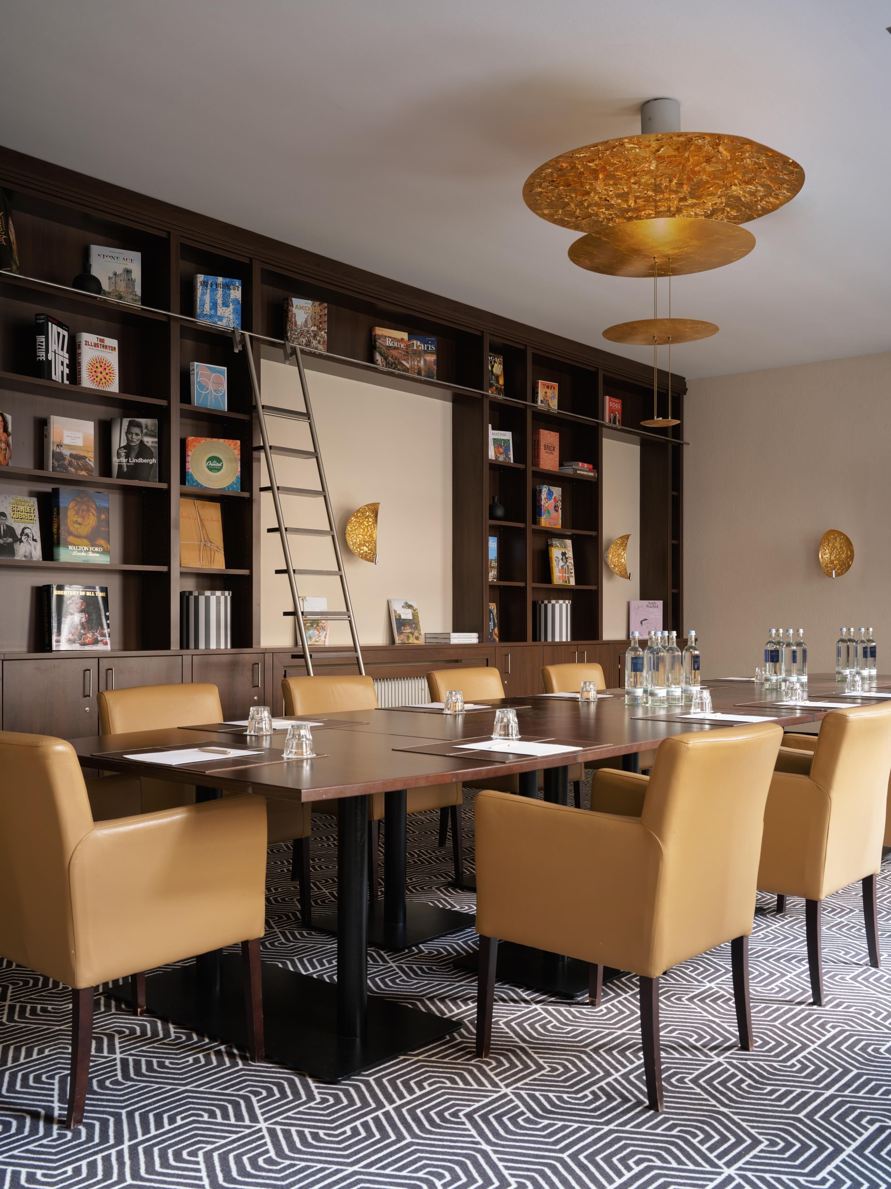 A conference room with a long table, multiple chairs, a bookshelf, and a decorative ceiling light fixture.