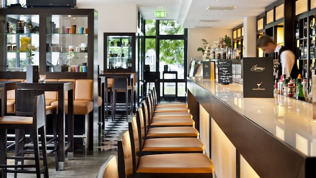 A bar area with seating, a bar counter, and shelves with bottles. - Flemings Hotel München Schwabing (Munich)