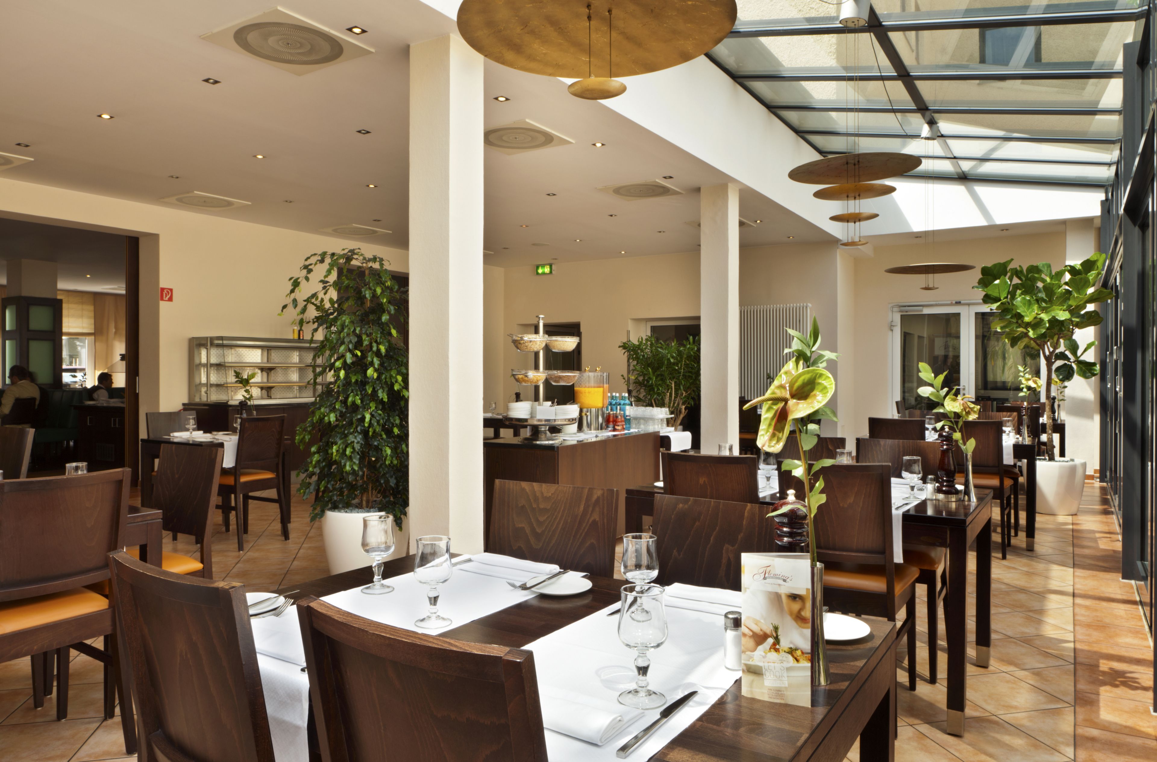 Un comedor moderno con mesas dispuestas para comensales, una zona de bar y una planta grande en maceta.