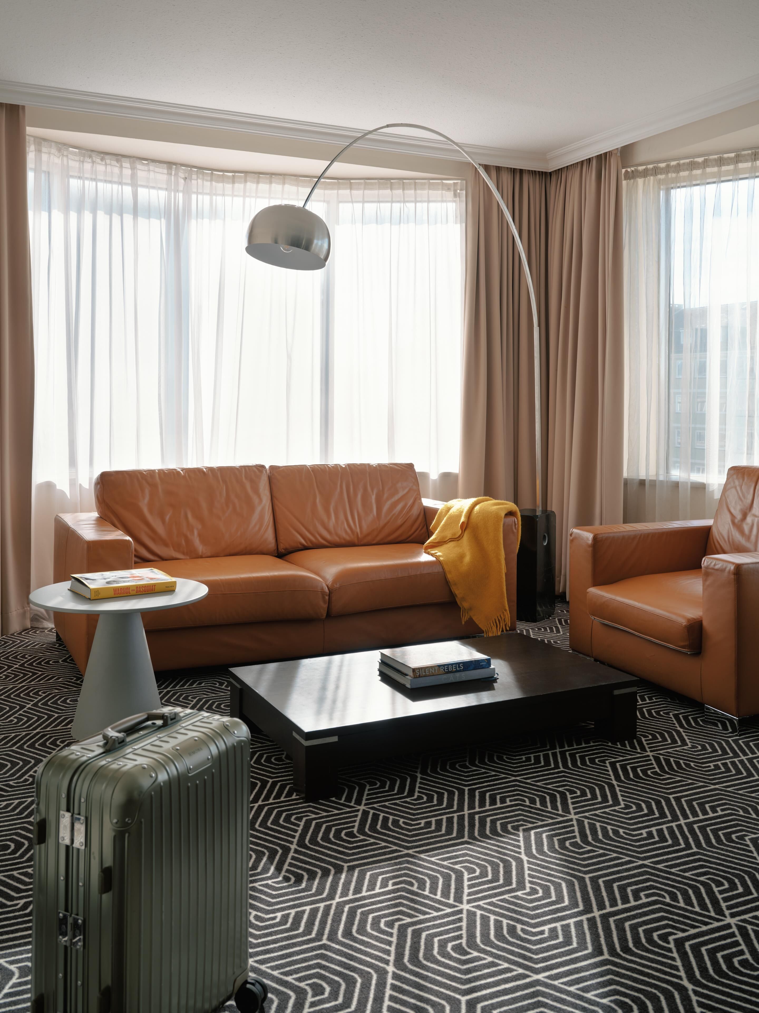A modern hotel room with a leather sofa, a coffee table, a lamp, and a patterned floor.