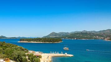 Un resort costero con playa, muelle para barcos y montañas al fondo.