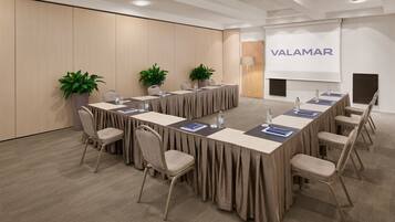 Uma sala de conferências com uma mesa comprida, cadeiras e uma tela de projetor exibindo "VALAMAR".