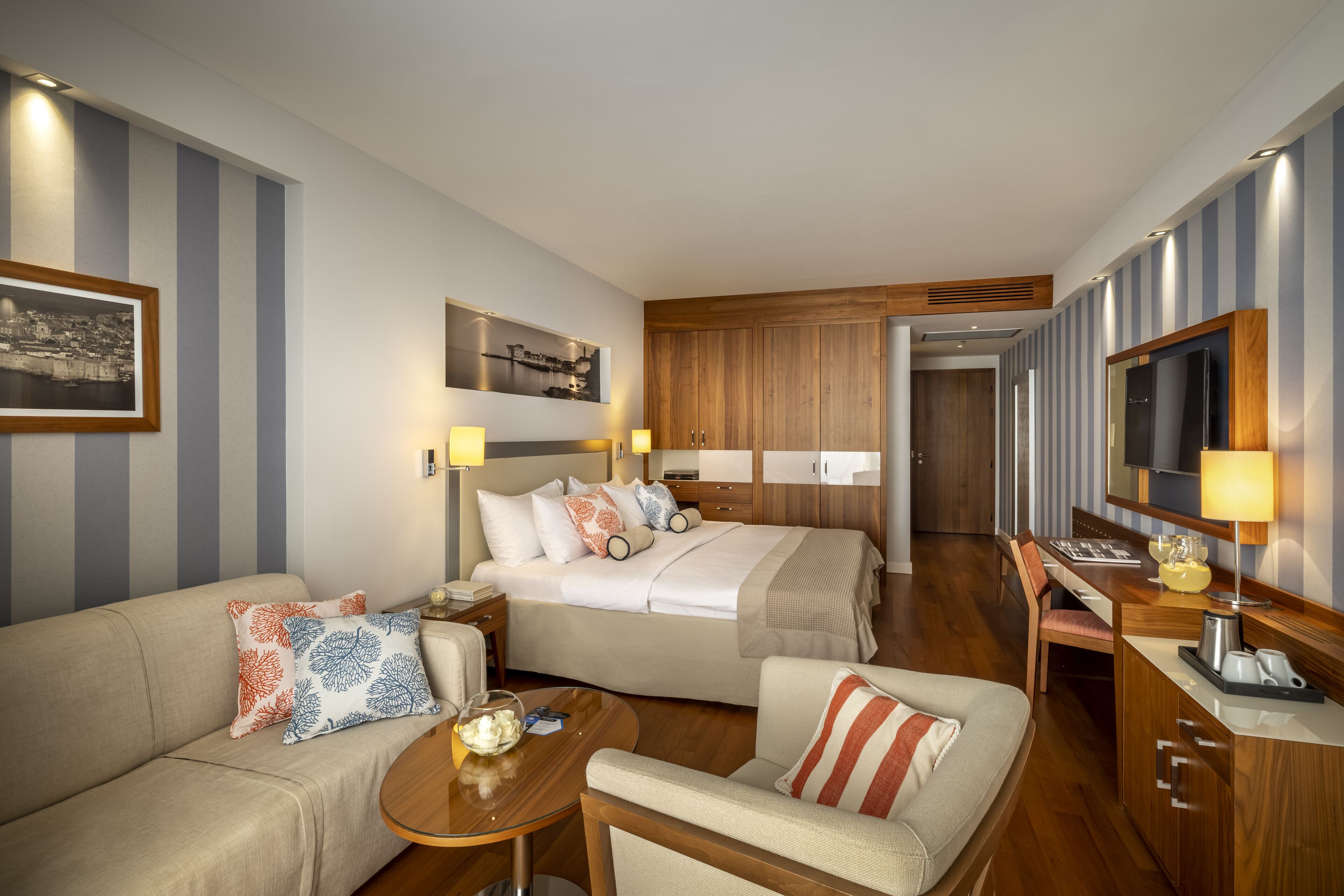 Une chambre d’hôtel avec un lit, un canapé, une petite table, une télévision et une armoire en bois.